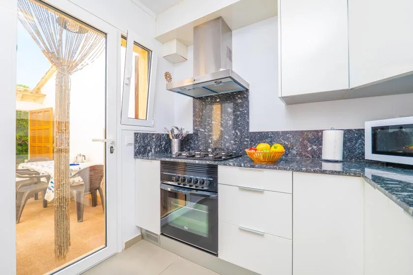 A bright kitchen with white cabinets, a cooktop, and a window overlooking a patio.
