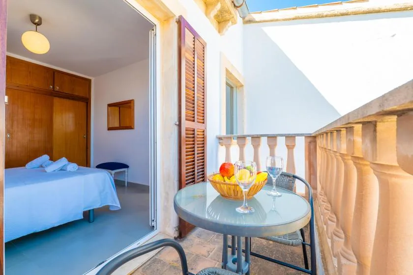 A bedroom opens onto a balcony with a glass table and fruit bowl.