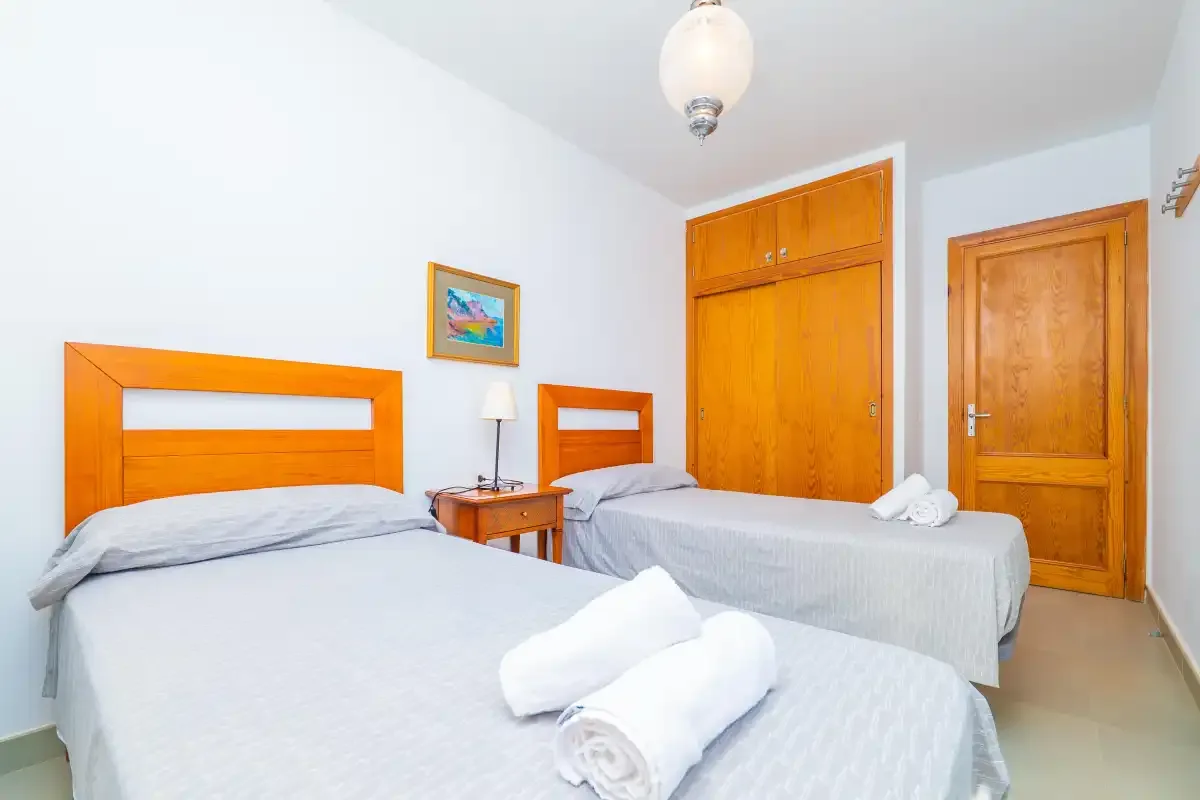 A bedroom with two beds, wooden wardrobes, and a bedside table.