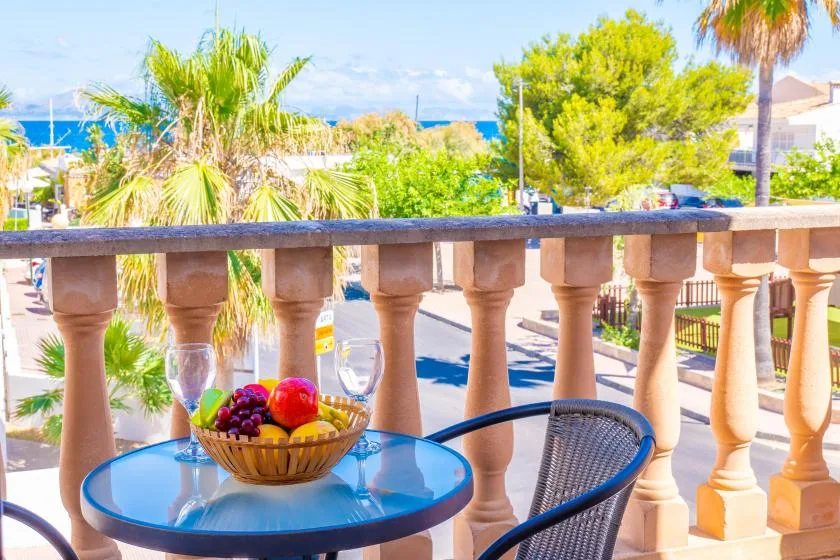 A balcony seating area overlooks palm trees, greenery, and the sea.