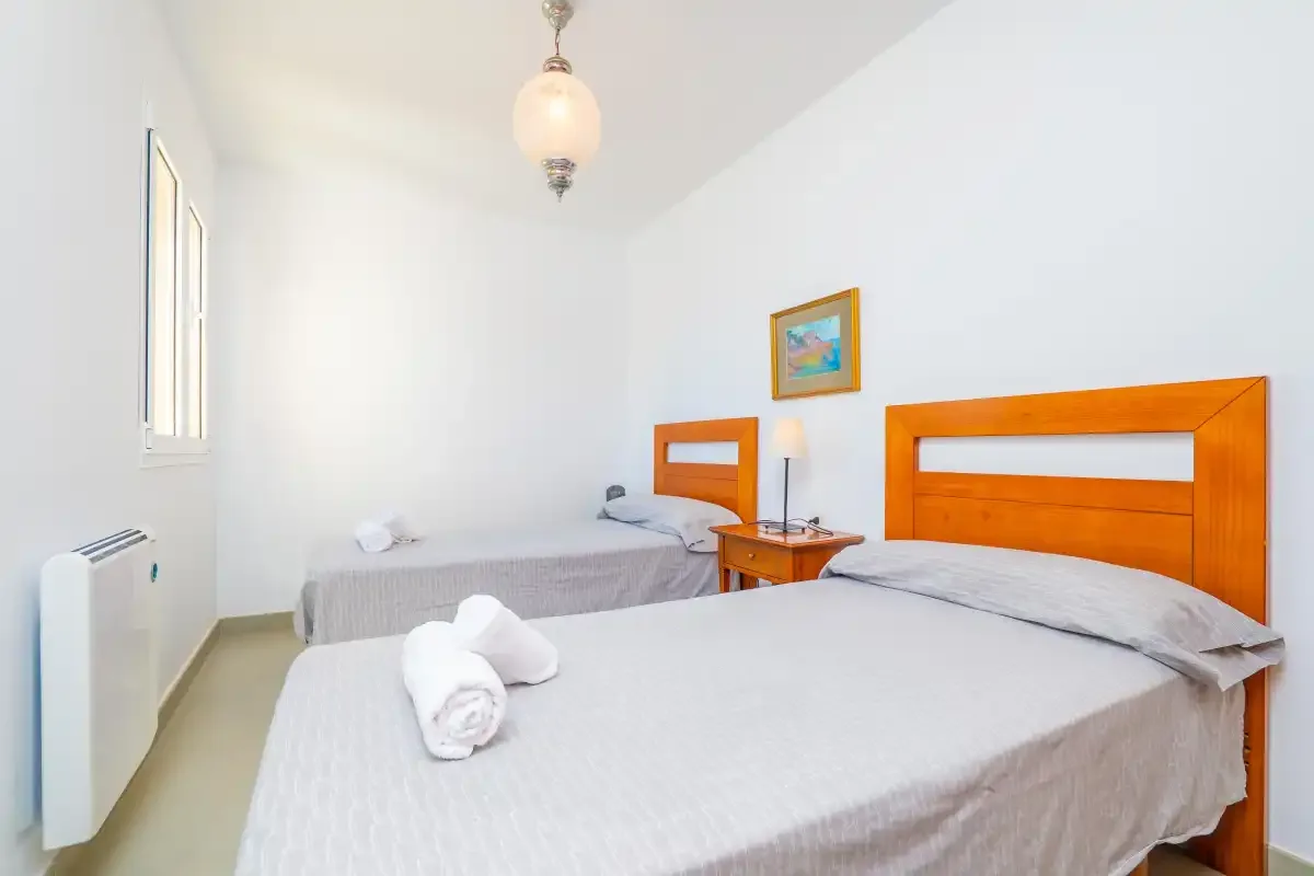 A bright bedroom with two beds and a small bedside table.