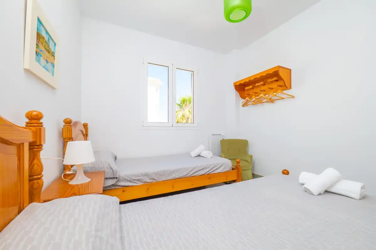 A bright bedroom with beds, a small bedside table, and a window.