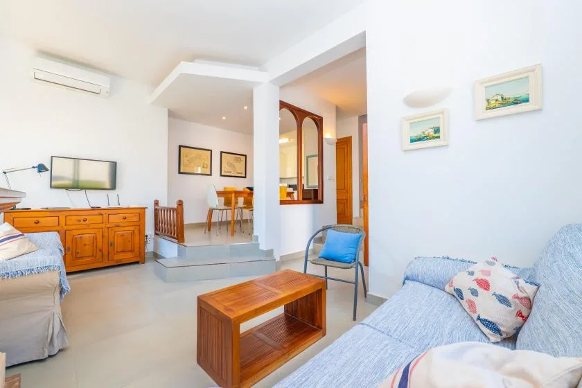 A bright living room with seating, a wooden coffee table, and a dining area beyond.