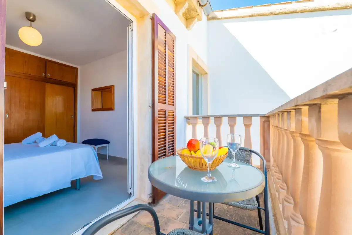 A balcony seating area beside an open bedroom with a bed and wooden wardrobe.