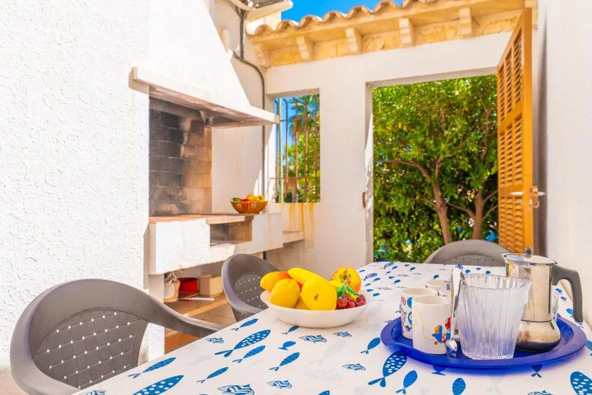 A dining area opens onto a leafy garden, with a table beside a built-in grill.