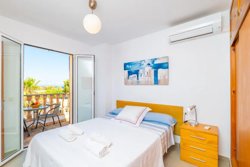 A bright bedroom with a neatly made bed and an open balcony door.