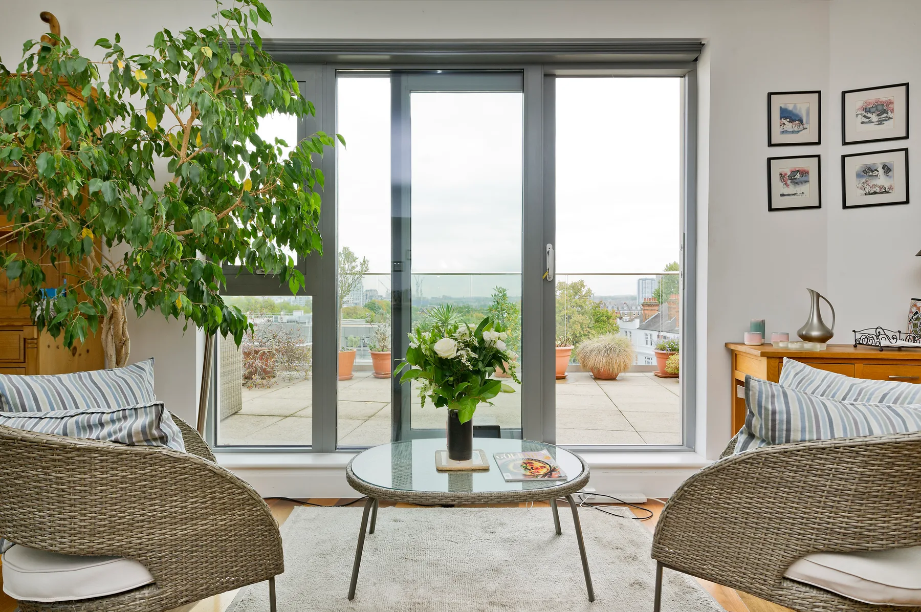 Una sala luminosa con asientos, una mesa de centro de vidrio y grandes ventanales con vista a una terraza.