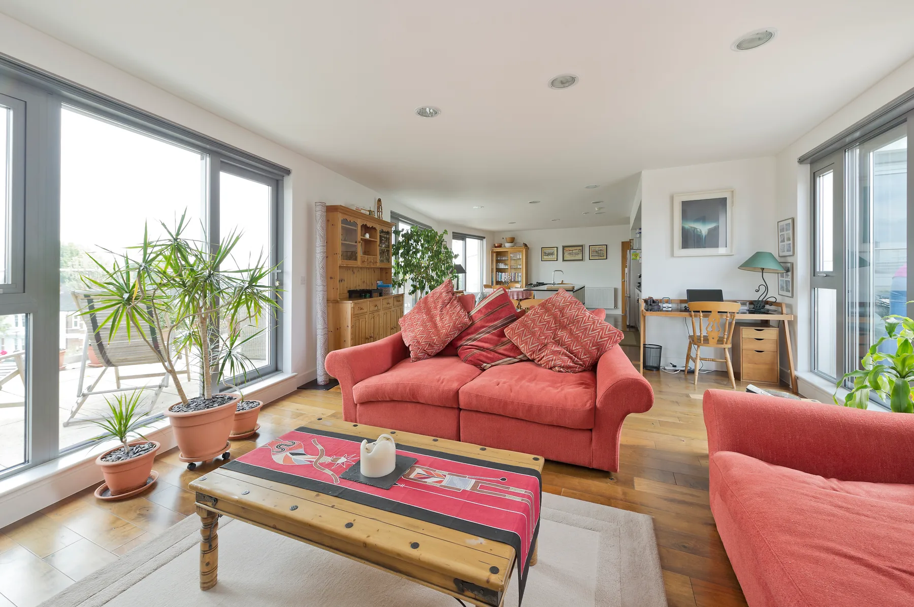 Una sala luminosa con asientos rojos, una mesa de centro de madera y grandes ventanales.