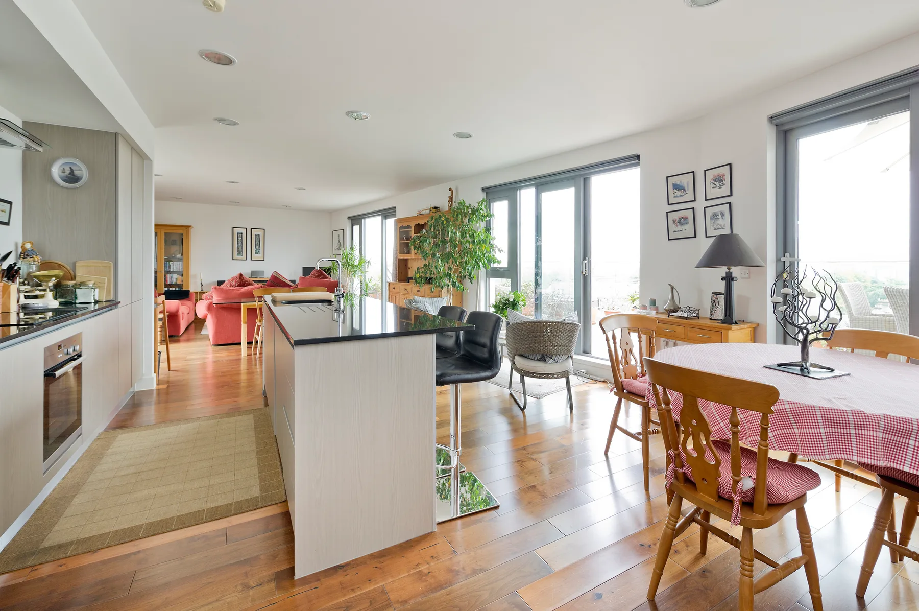 Una luminosa cocina y comedor de planta abierta, con grandes ventanas y suelo de madera.