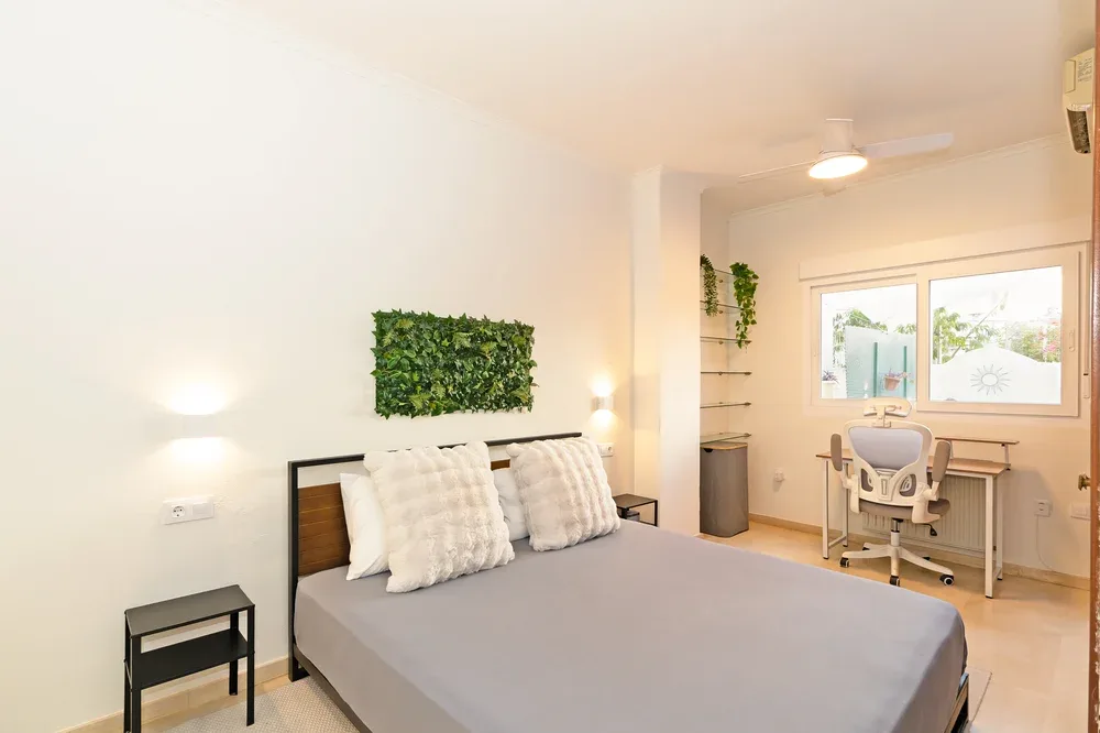 A bedroom with a bed, desk, and large window.
