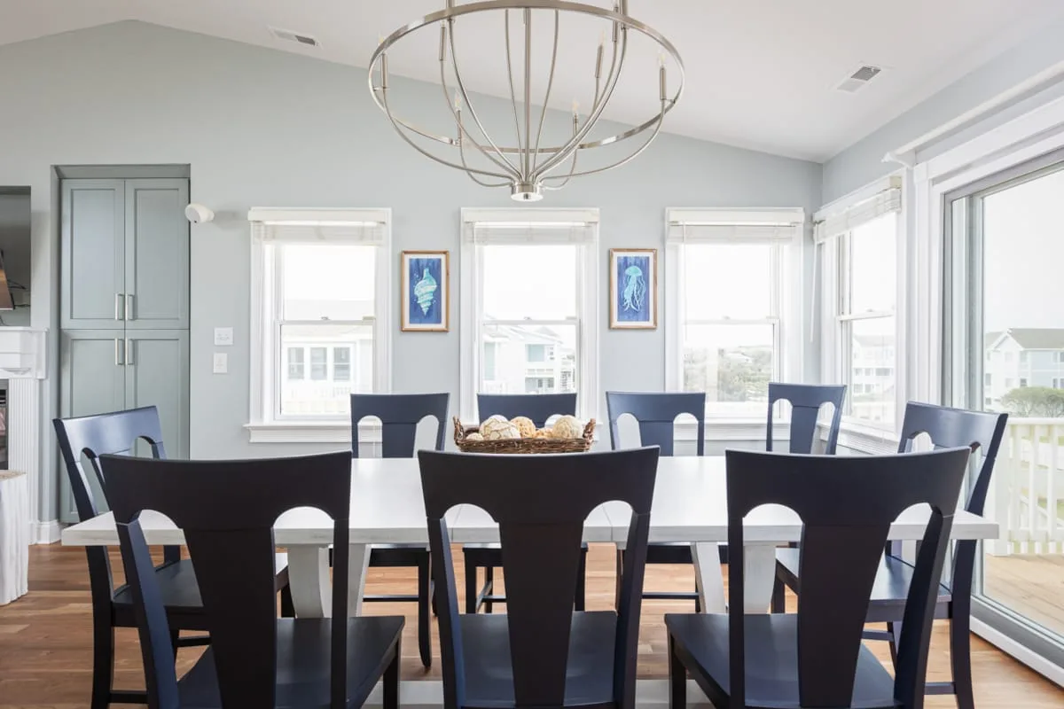 Un comedor luminoso con una mesa larga y sillas oscuras bajo una lámpara colgante.