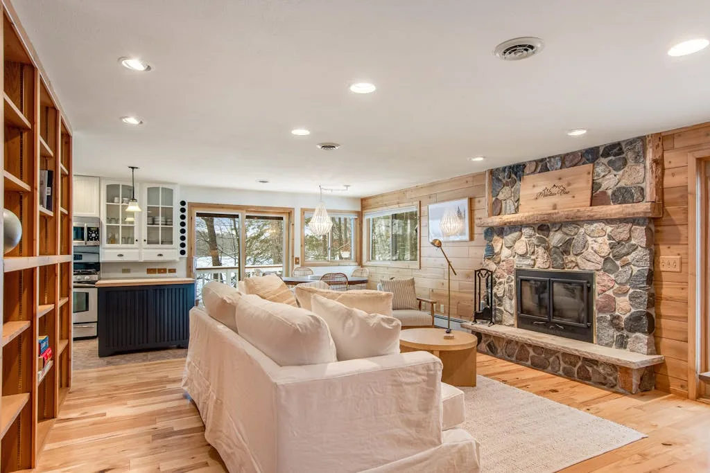 A living room with seating arranged around a stone fireplace and wooden shelving.