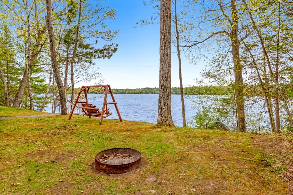 A lakeside yard with a wooden swing and a fire pit.