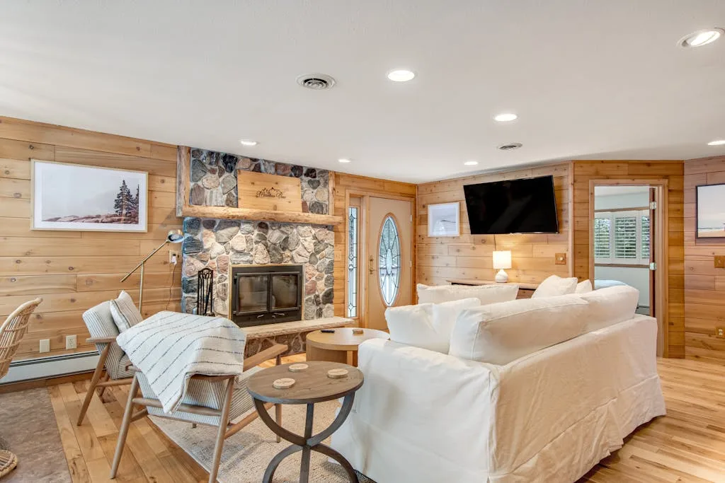 A wood-paneled living room with white seating and a stone fireplace.