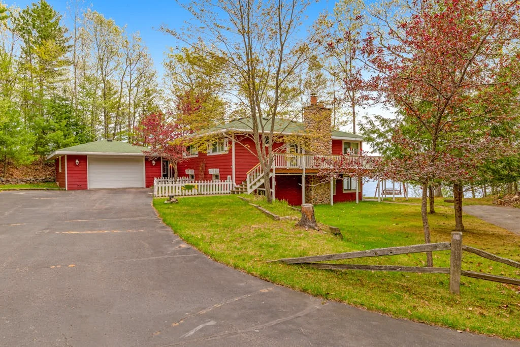 A red house and detached garage sit beside a paved driveway and green lawn.
