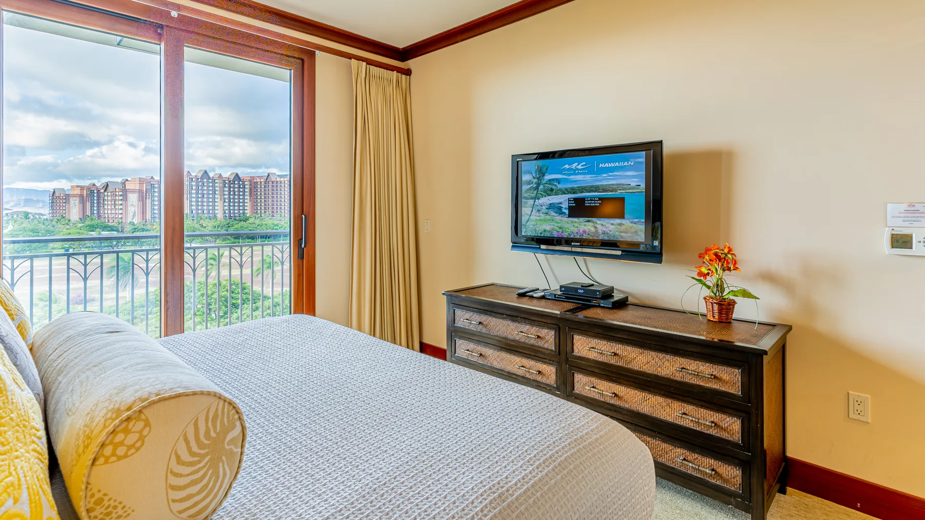 Un dormitorio con una cama, un televisor sobre una cómoda y una puerta de vidrio que da a un balcón.