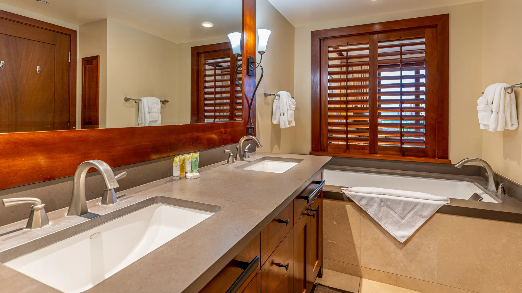 Un tocador de baño con dos lavabos, un espejo y persianas de madera.