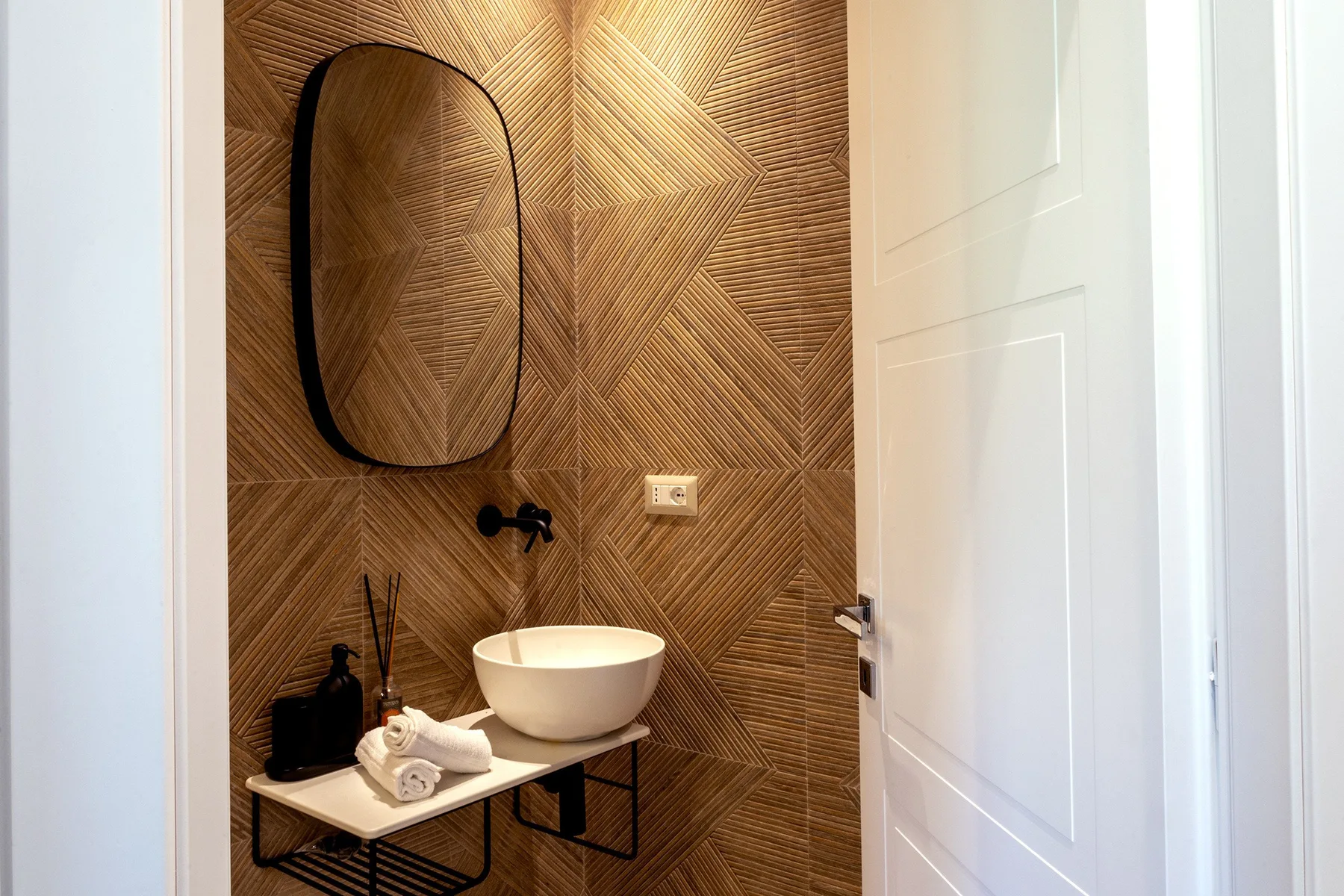 A bathroom vanity with a vessel sink stands against a patterned brown wall.