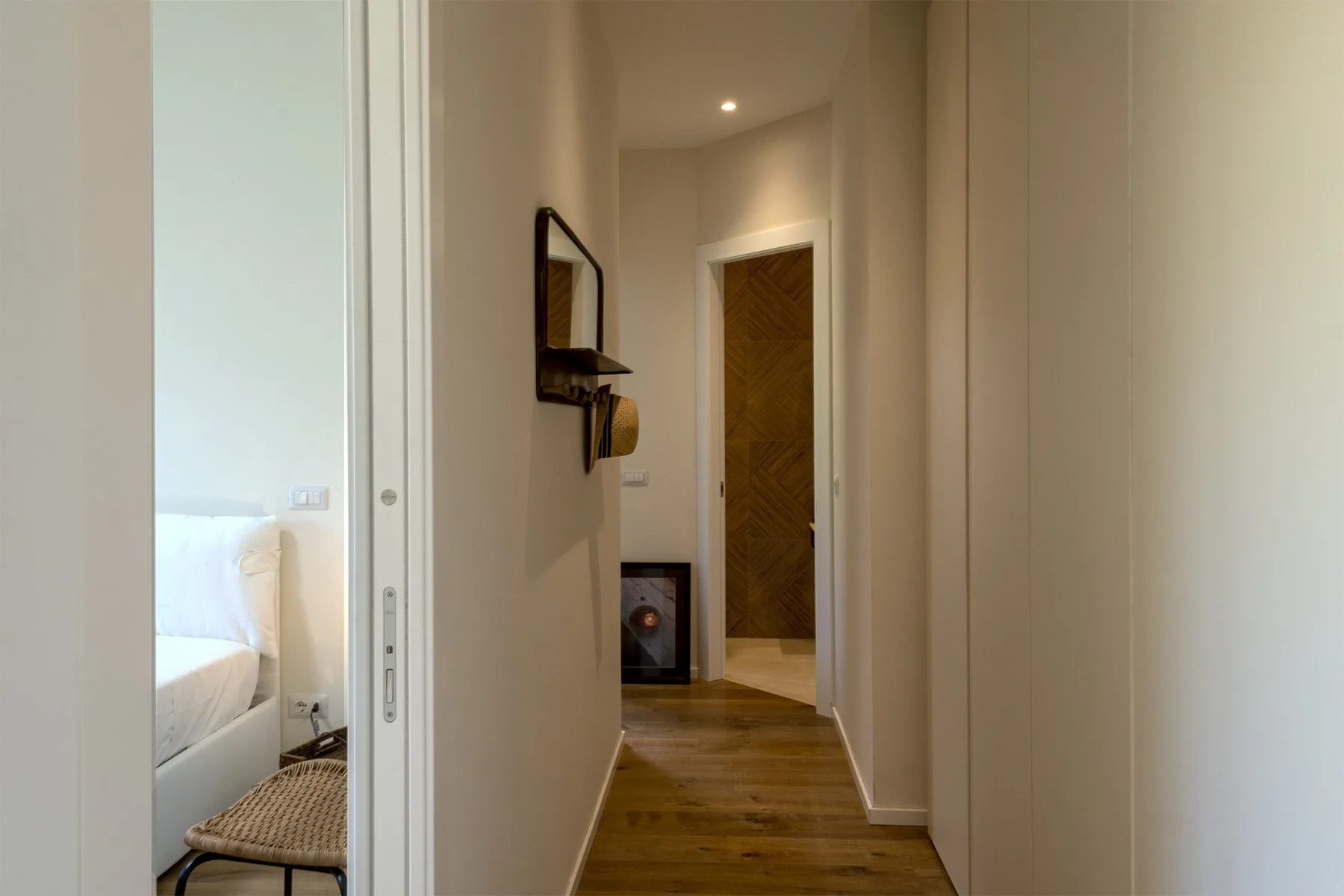 A narrow hallway with wood flooring leads to a closed wooden door.