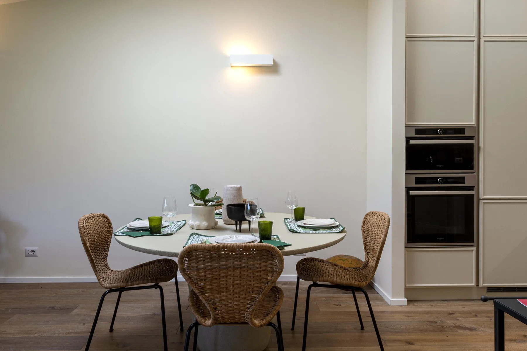 Dining area with a set table and woven seating beside built-in appliances.
