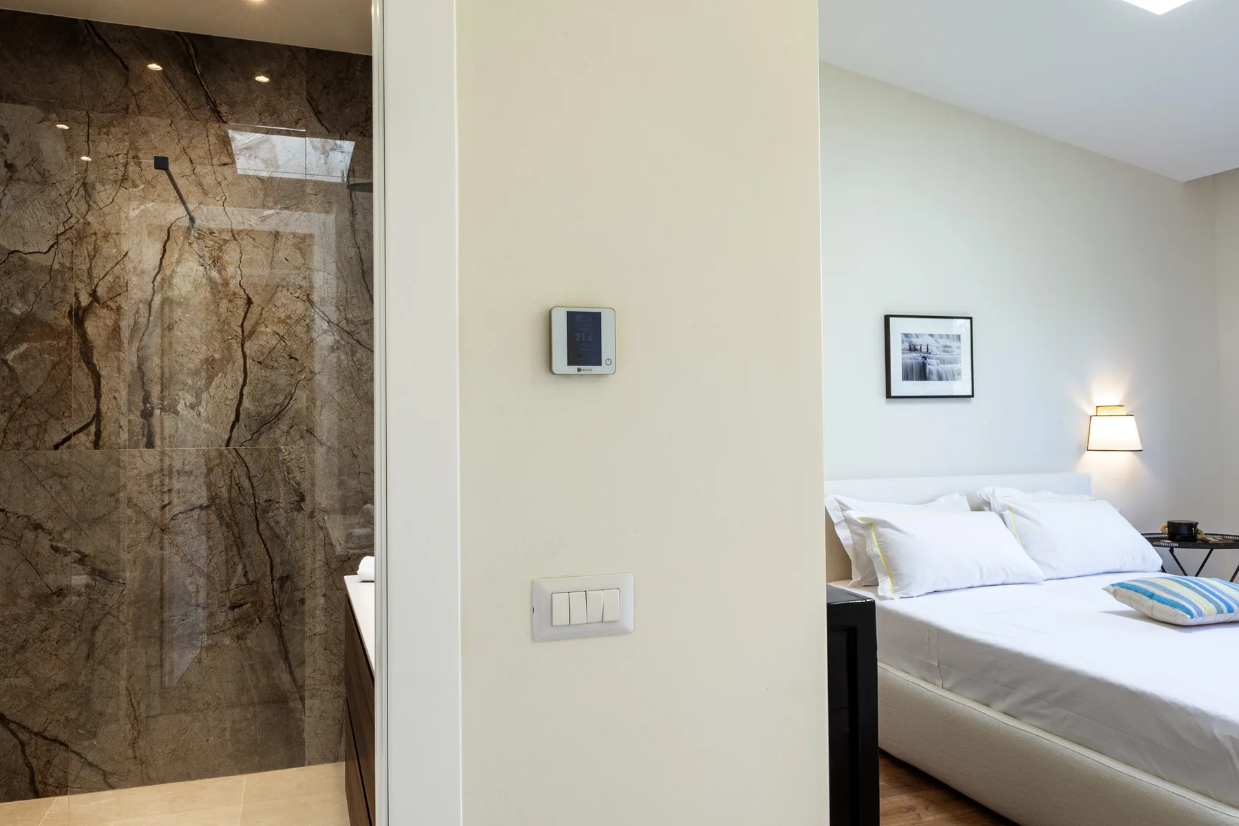 A bedroom with a bed beside a bathroom with a glass shower.