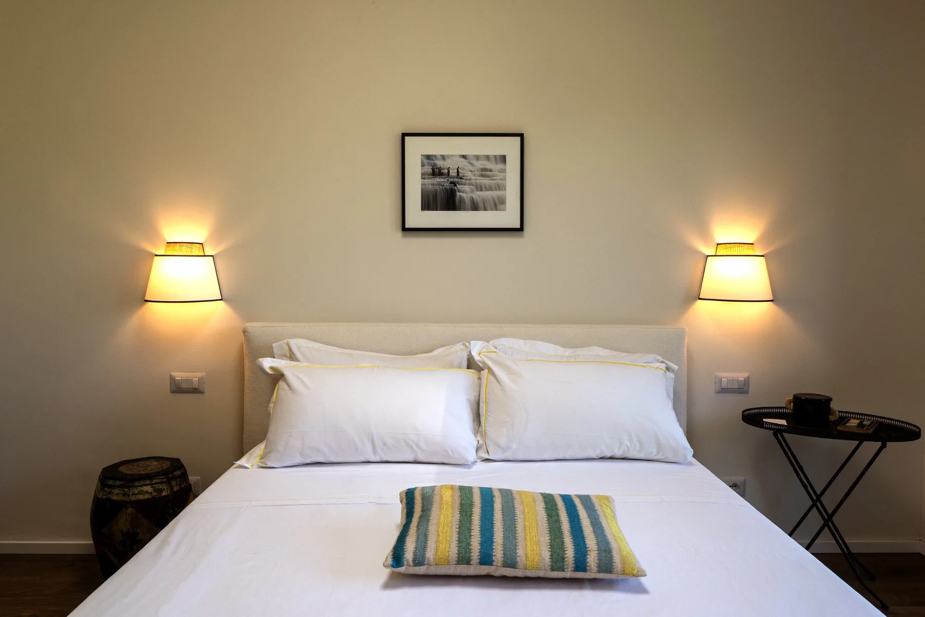 Bedroom with a neatly made bed, striped cushion, and matching wall lamps.