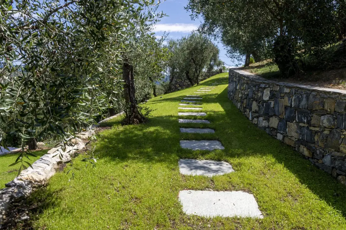 A grassy garden path with stepping stones runs beside a stone retaining wall.