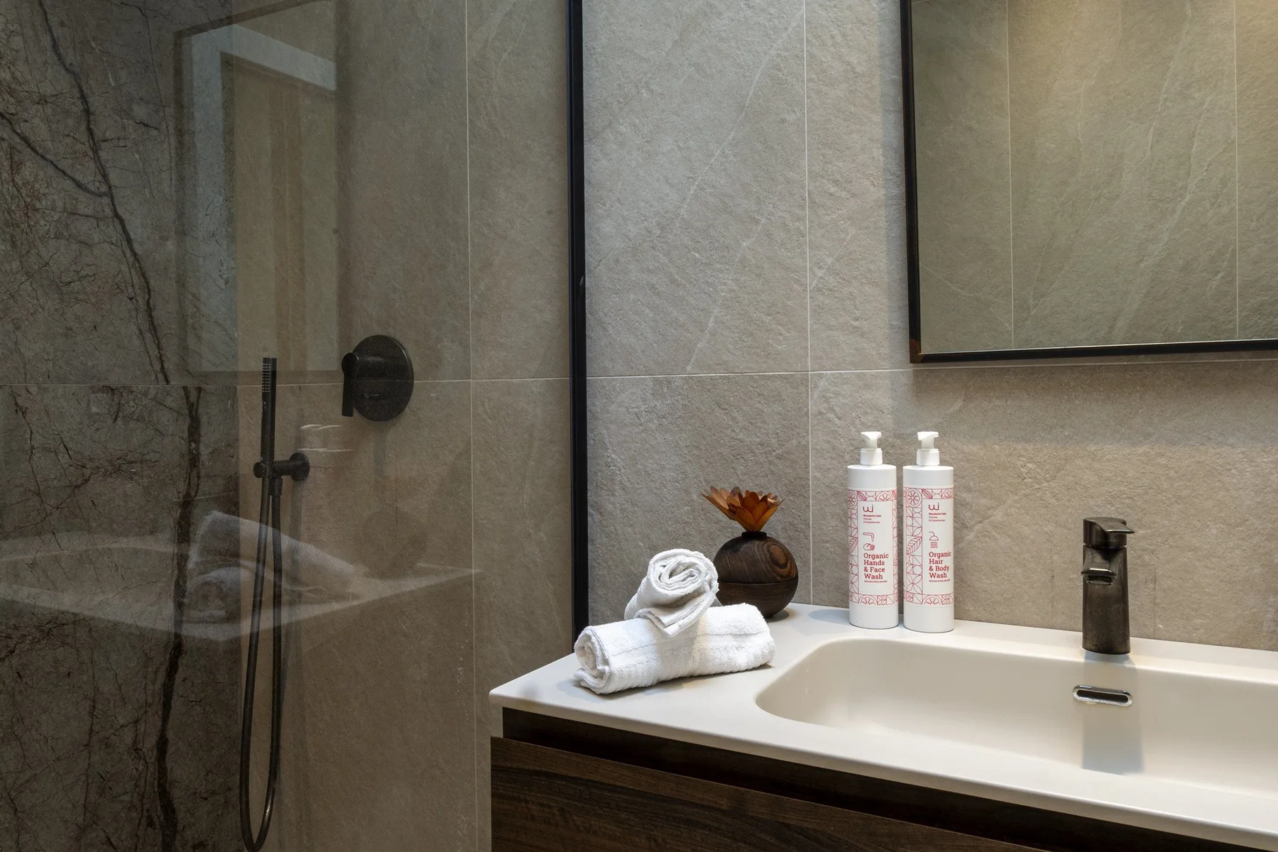 A bathroom vanity with a sink, toiletries, and folded towels beside a shower.