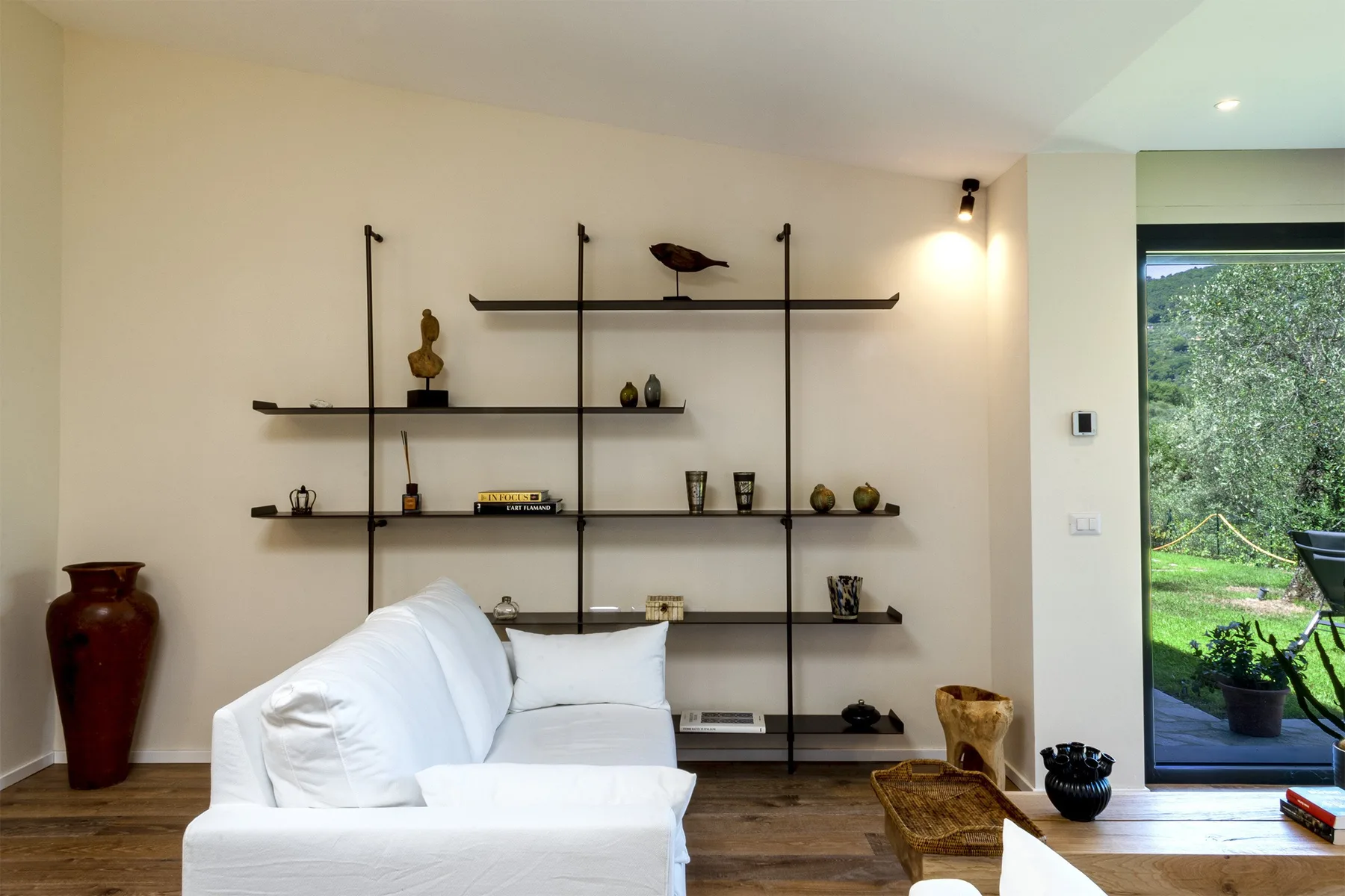 A bright living room with white seating and wall-mounted display shelves.