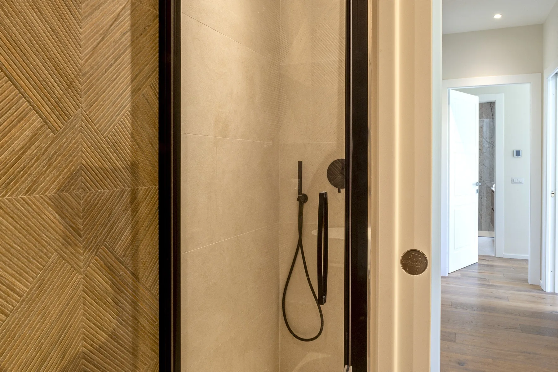A bathroom shower area with a handheld shower and patterned wall tiles.