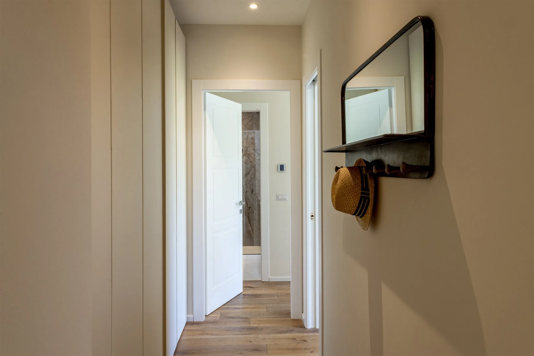 A hallway with wood-look flooring and a mirror above a wall shelf.