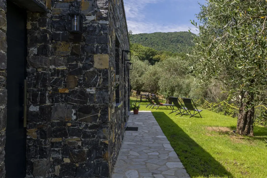A stone building borders a paved path leading to outdoor seating on a grassy hillside.