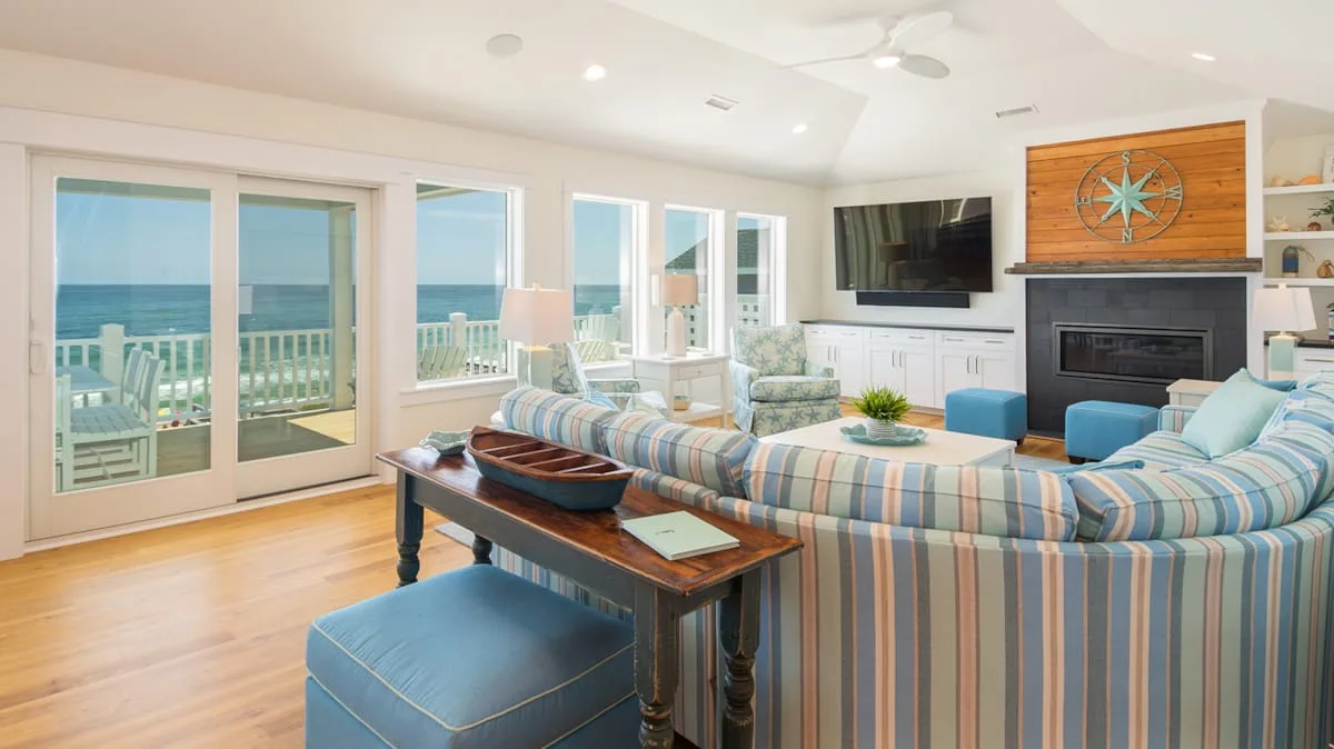 A bright living room with striped seating and wide windows overlooking the ocean.