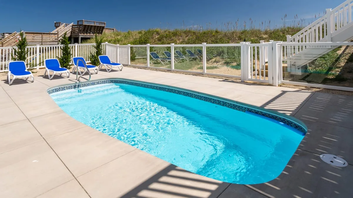 An outdoor swimming pool sits beside a paved deck with blue lounge chairs.