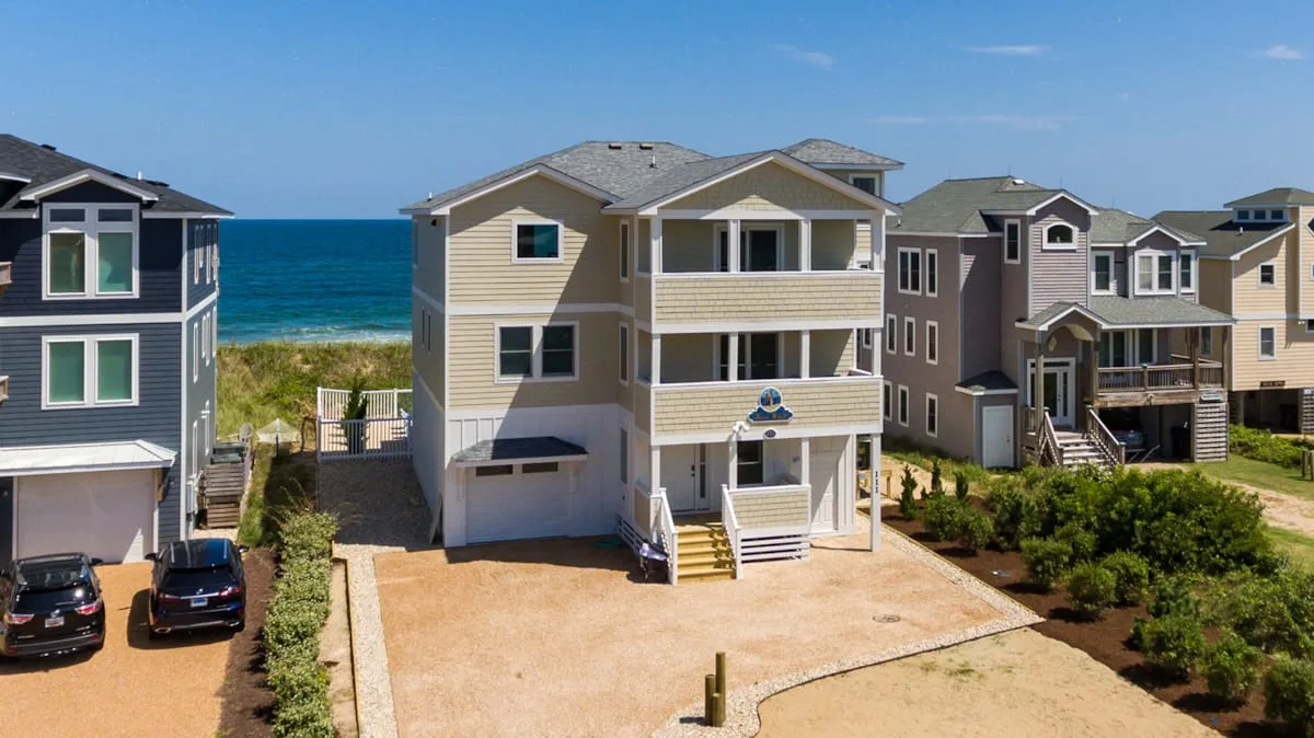 A row of beachside houses faces a sandy lot, with the ocean visible beyond.