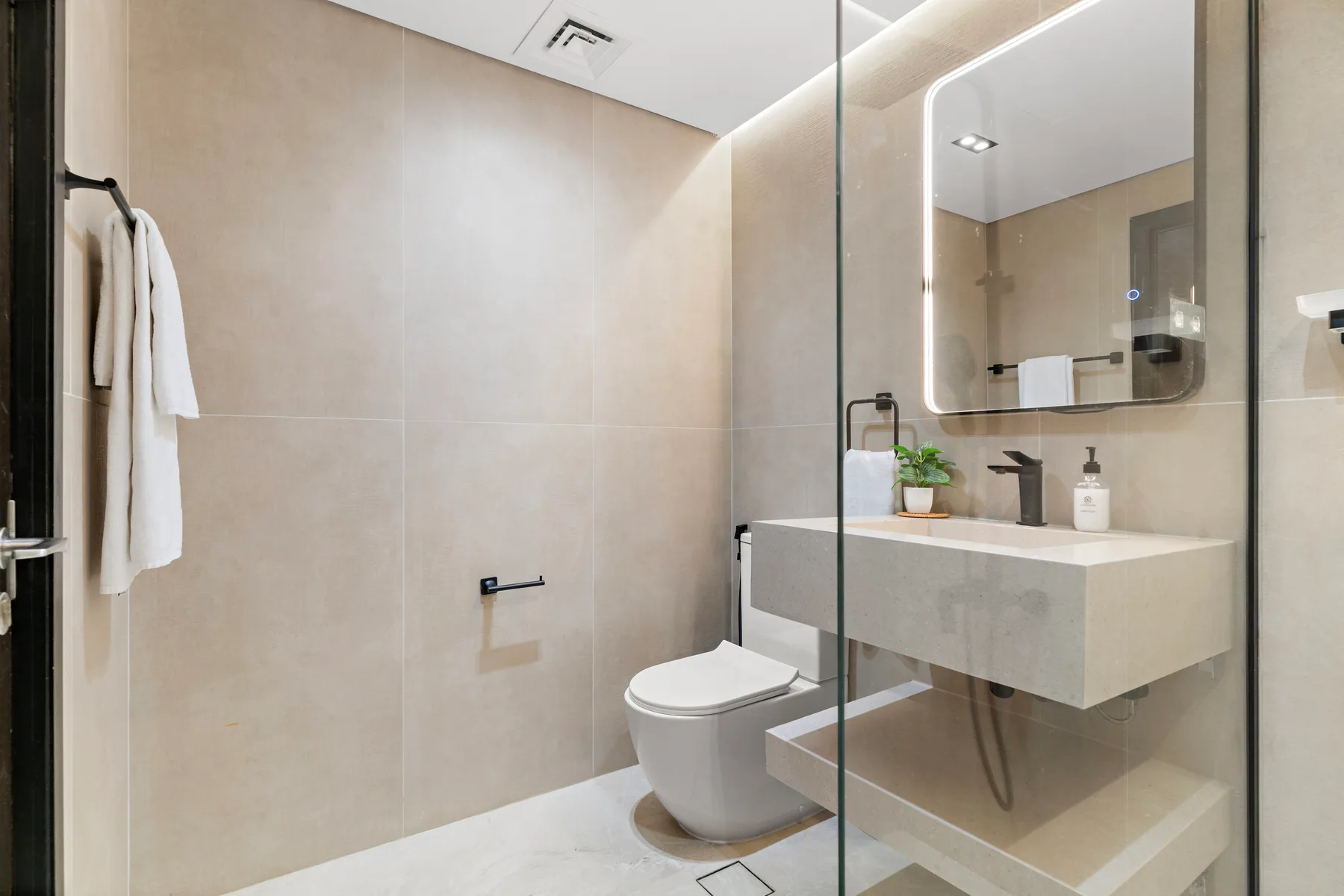 Un baño moderno con ducha de vidrio, inodoro y lavabo suspendido.