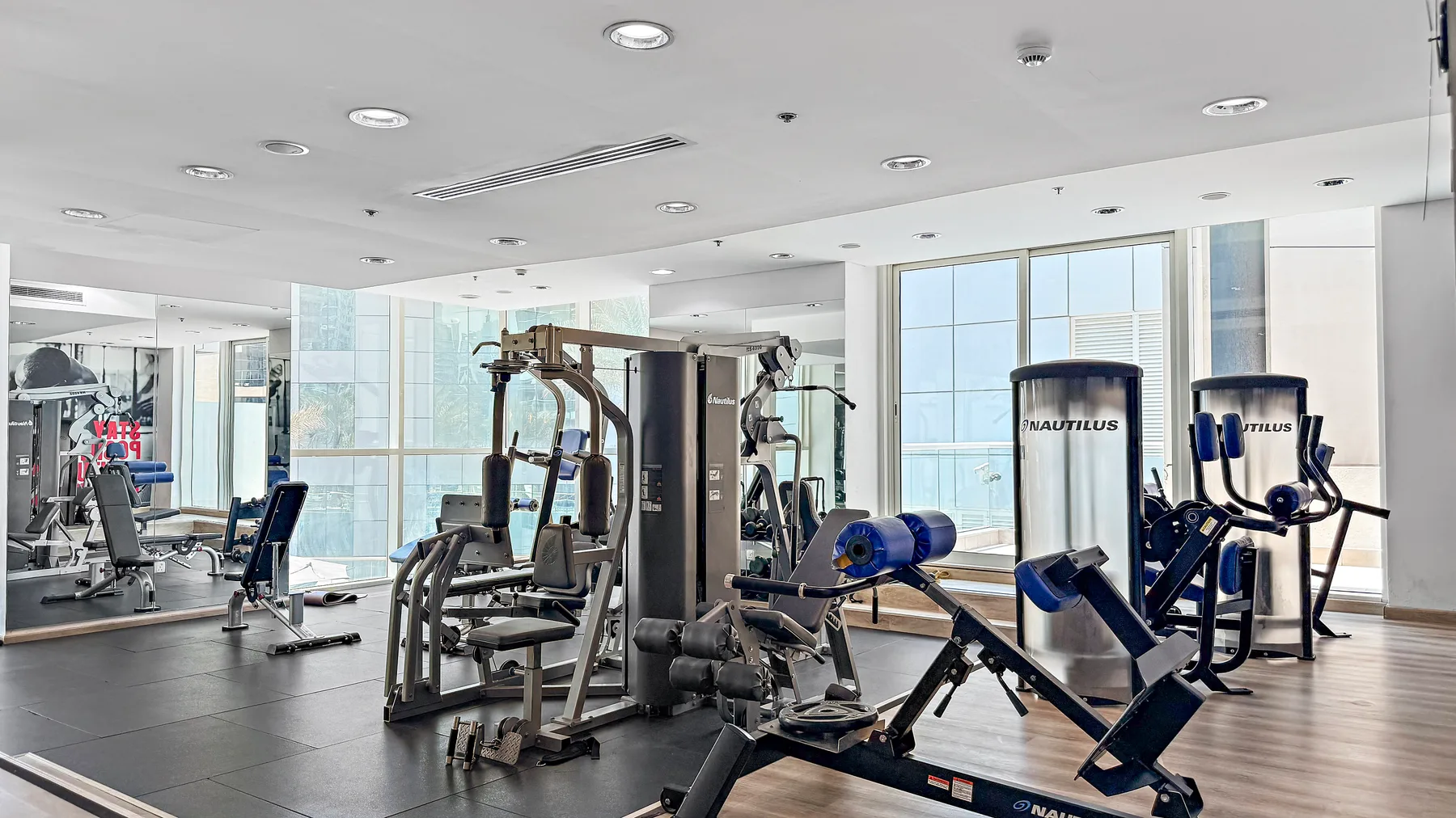 Un gimnasio luminoso con máquinas de ejercicio y grandes ventanas.