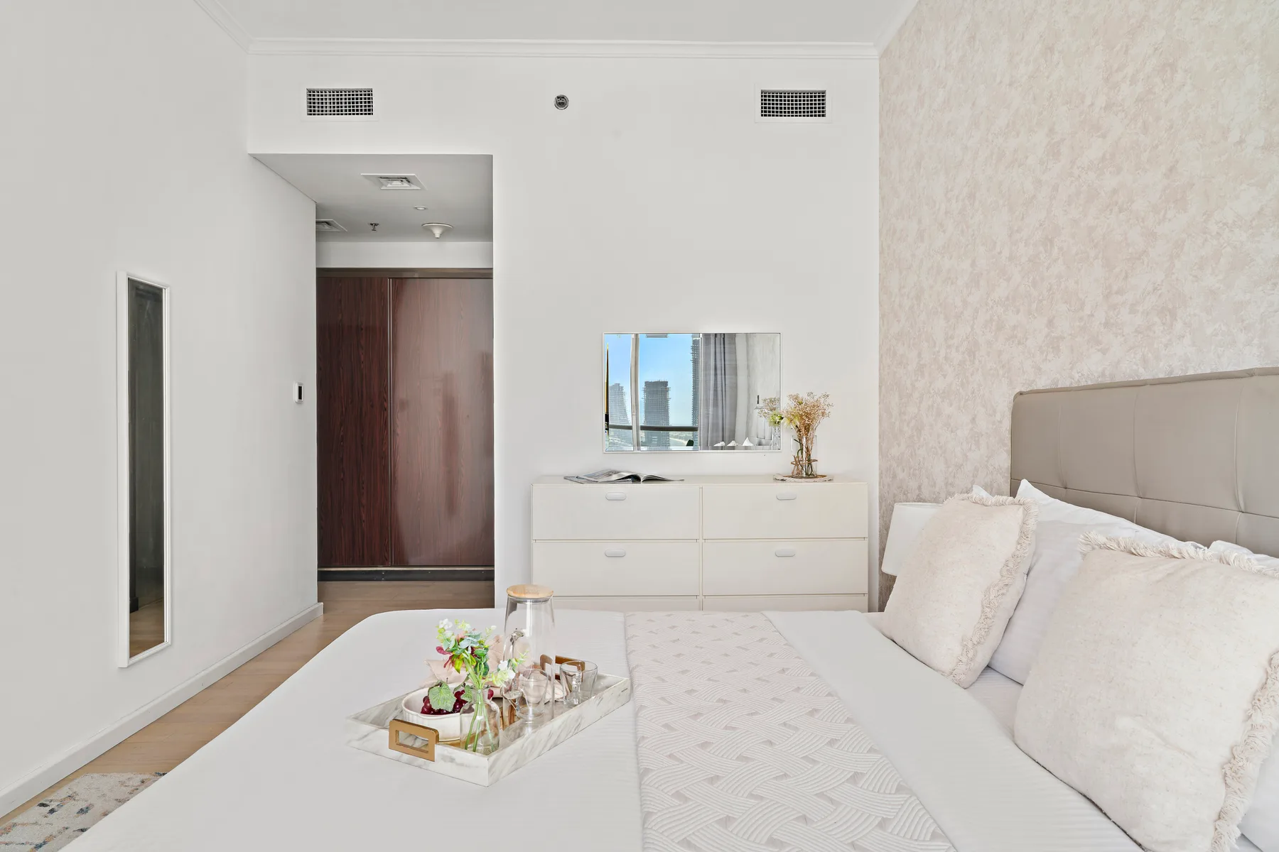 Un dormitorio luminoso con una cama, una cómoda y flores en una bandeja.