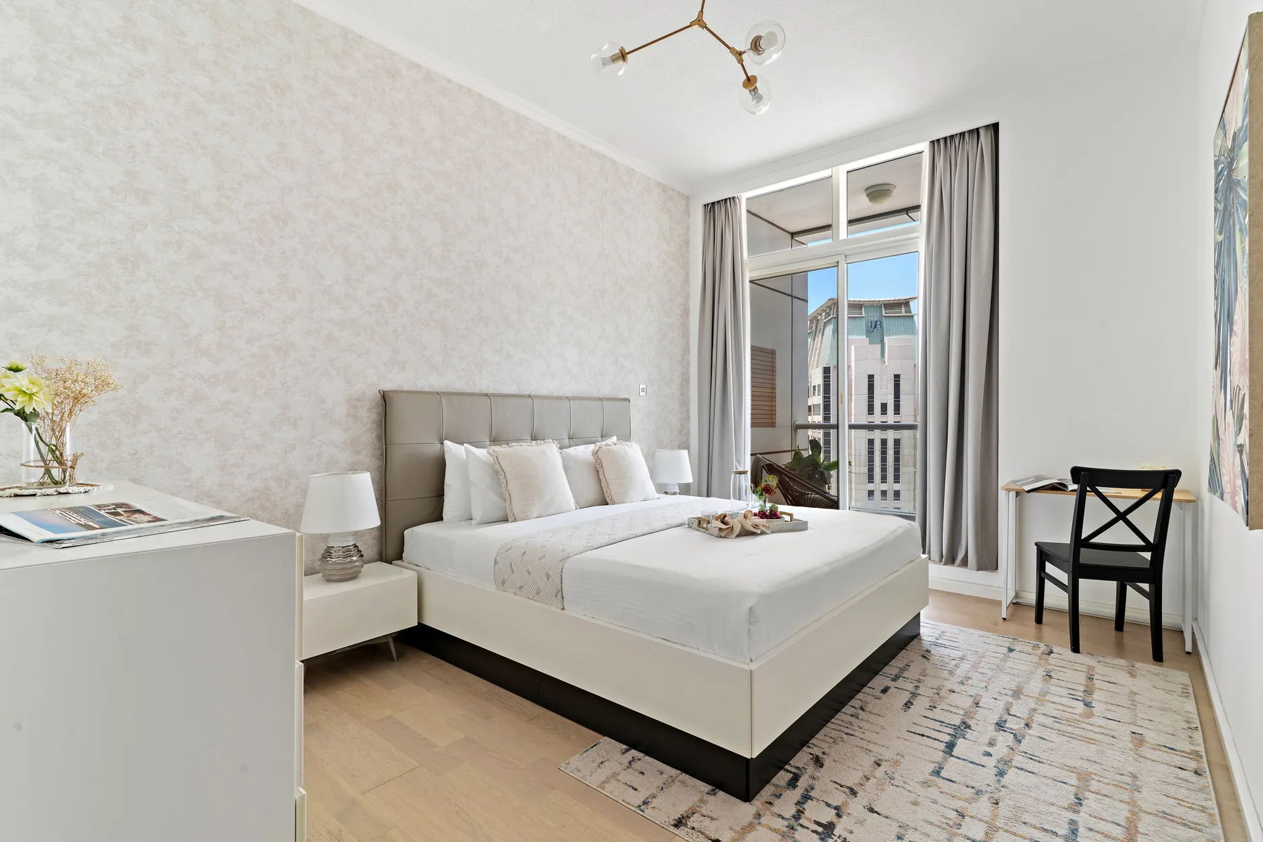 Dormitorio con una cama, una mesita de noche y ventanas altas con cortinas.