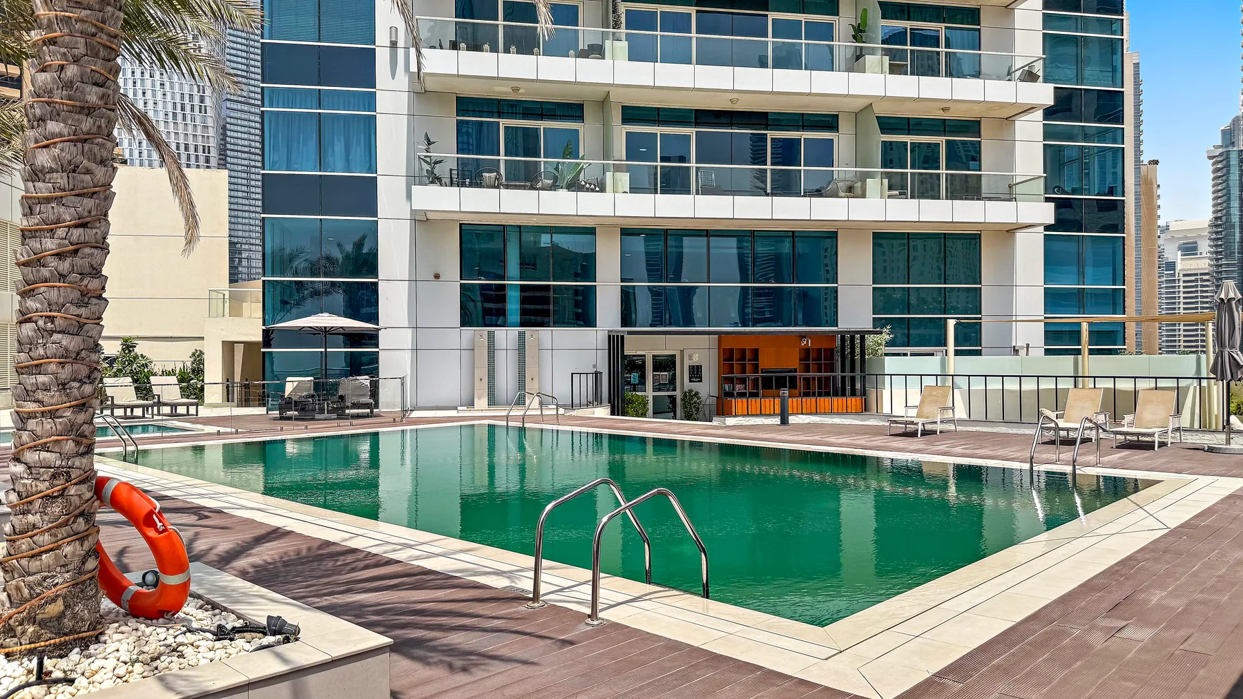 Una piscina está junto a un edificio moderno, con asientos junto a la terraza.