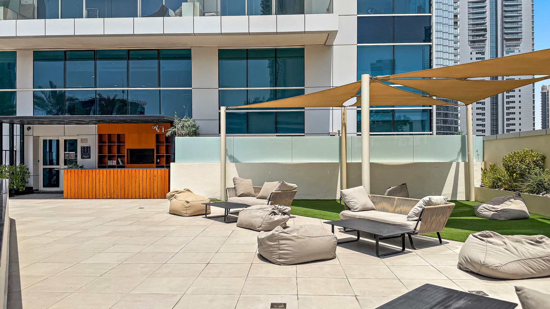 Una terraza exterior soleada tiene asientos acolchados bajo toldos.
