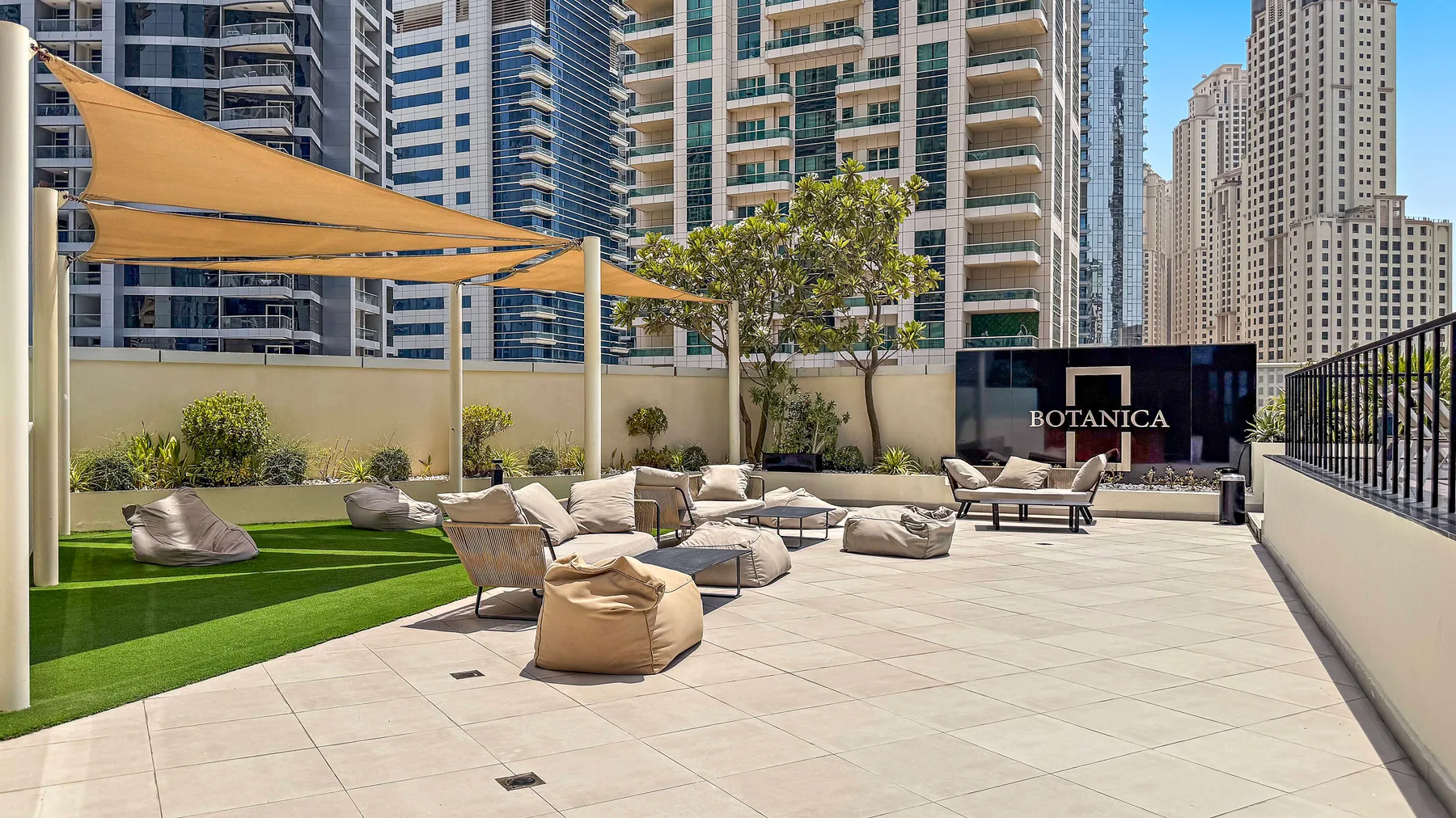 Una terraza en la azotea con asientos al aire libre, césped artificial y toldos entre edificios altos.