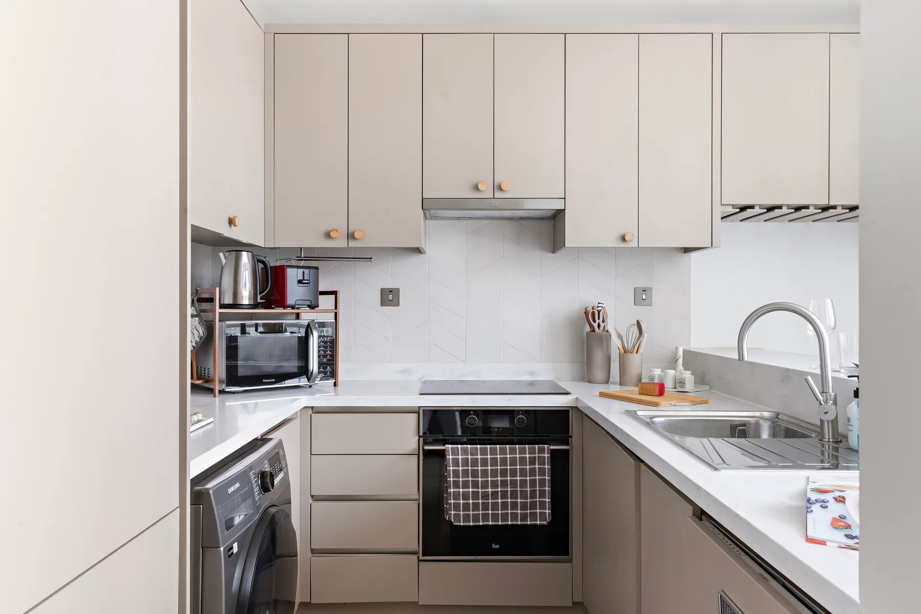 Una cocina moderna con gabinetes claros, encimera y electrodomésticos integrados.