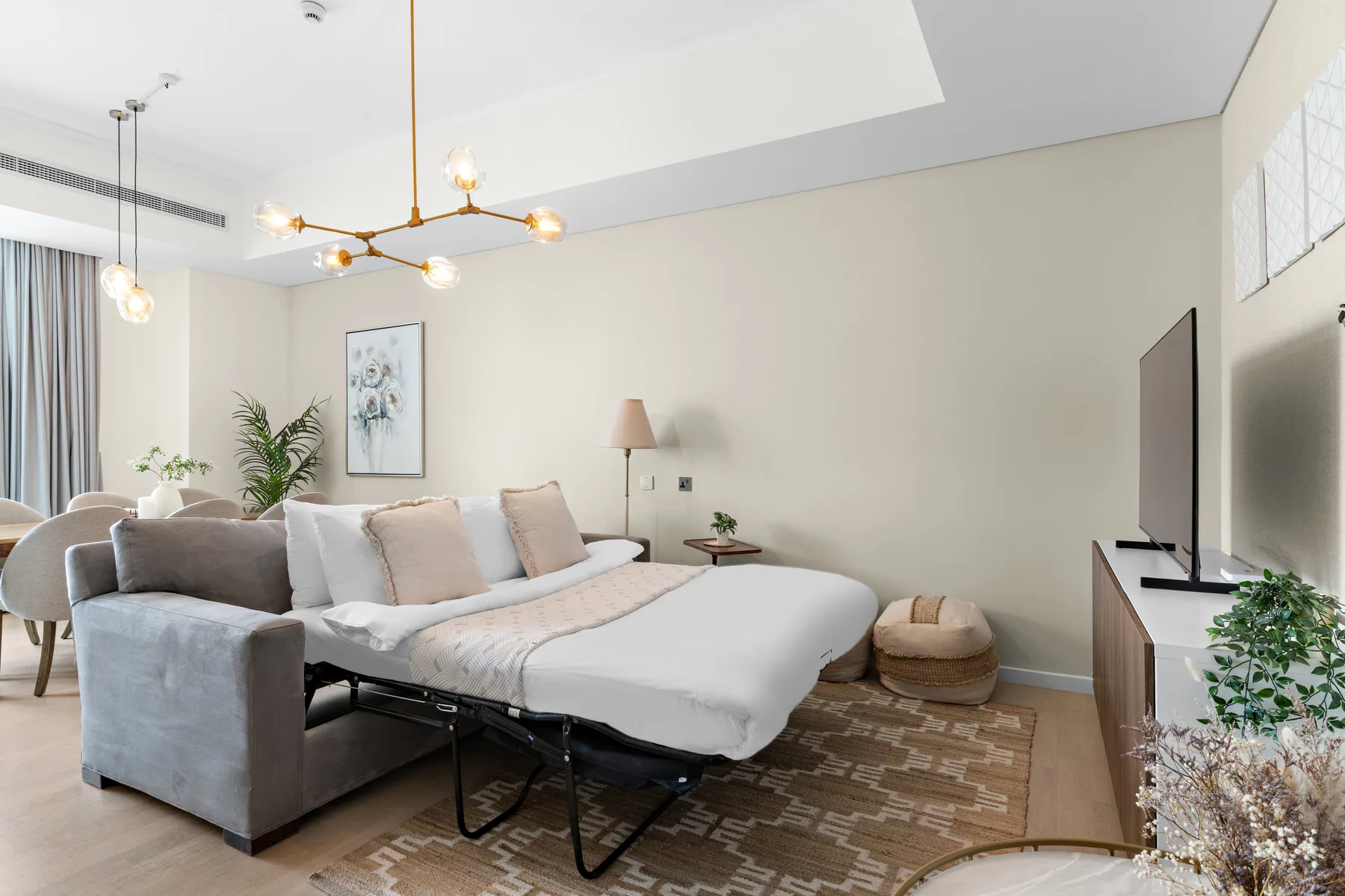 Una sala luminosa con un sofá dispuesto como cama bajo una lámpara moderna.