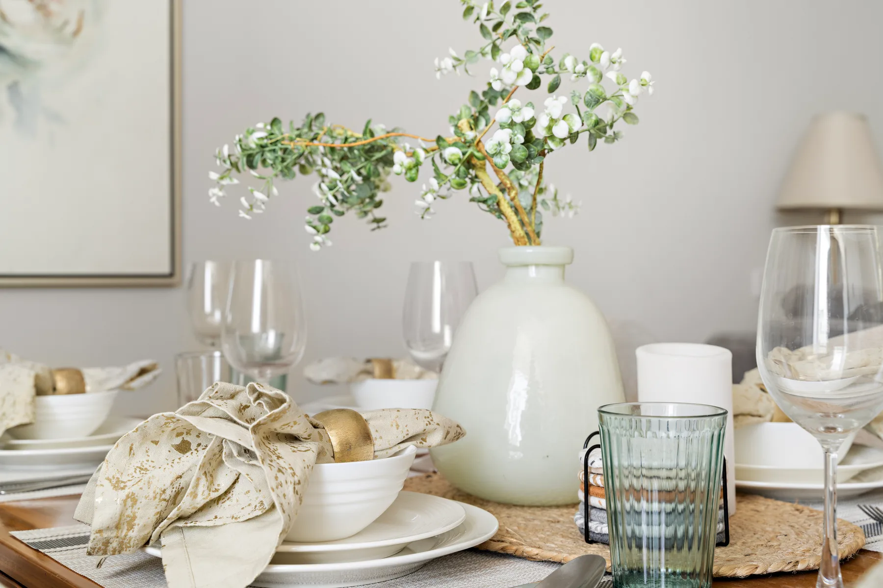 Una mesa de comedor está puesta con platos, vasos y un jarrón de flores.