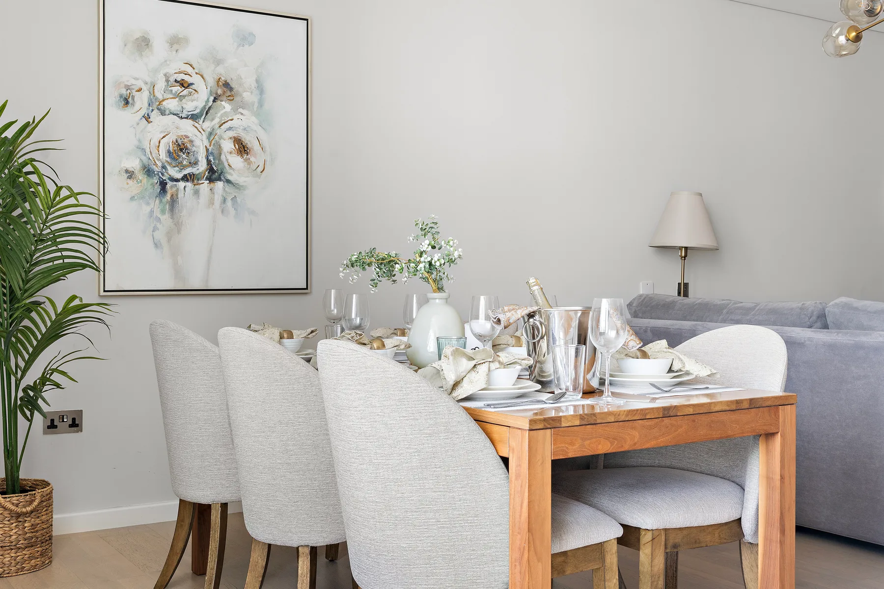 Comedor con una mesa puesta junto a asientos tapizados y un cuadro floral enmarcado.