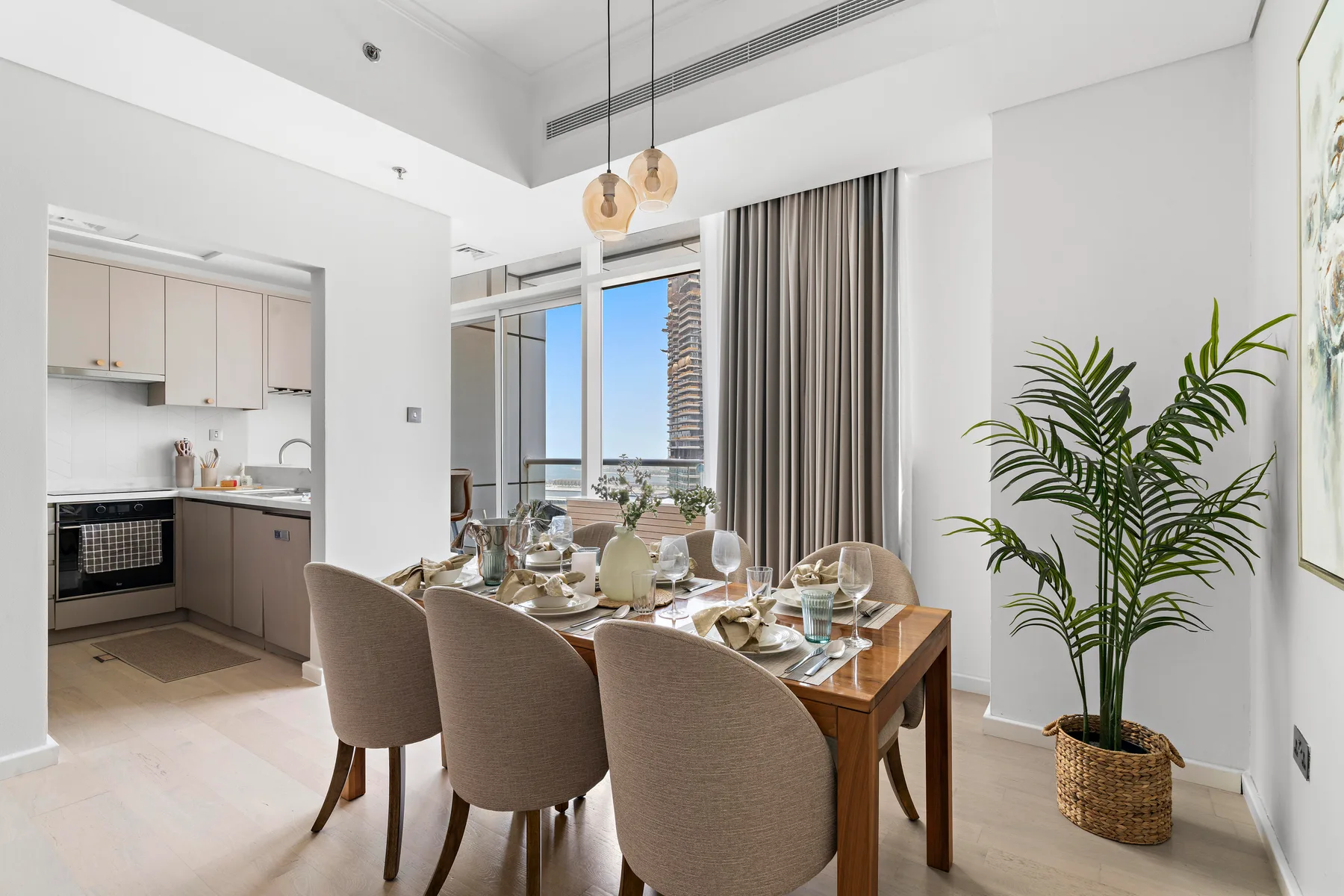 Un comedor luminoso con la mesa puesta junto a una cocina abierta y grandes ventanales.