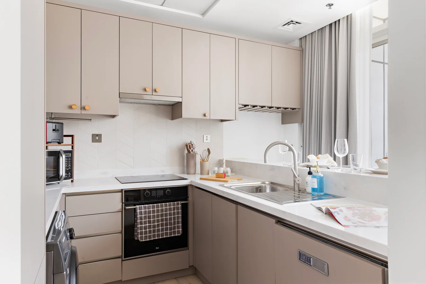 Una cocina luminosa con gabinetes claros, horno empotrado y fregadero junto a la ventana.