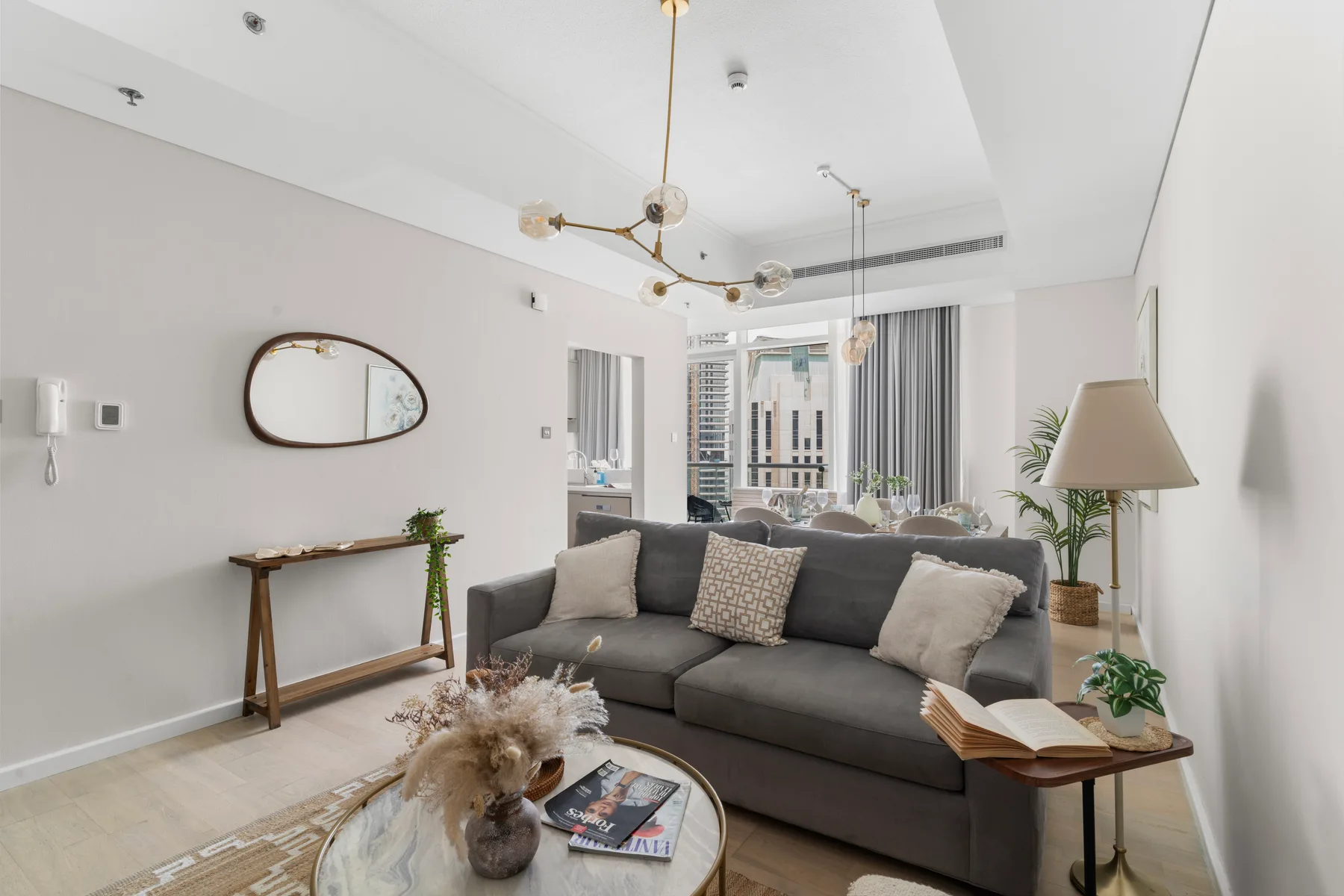 Una sala luminosa con asientos grises, una mesa de centro y ventanas altas.