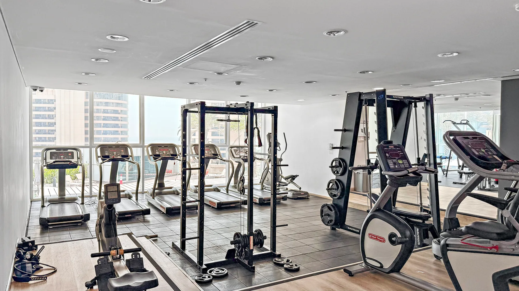 Un gimnasio con cintas de correr, máquinas de pesas y grandes ventanas.